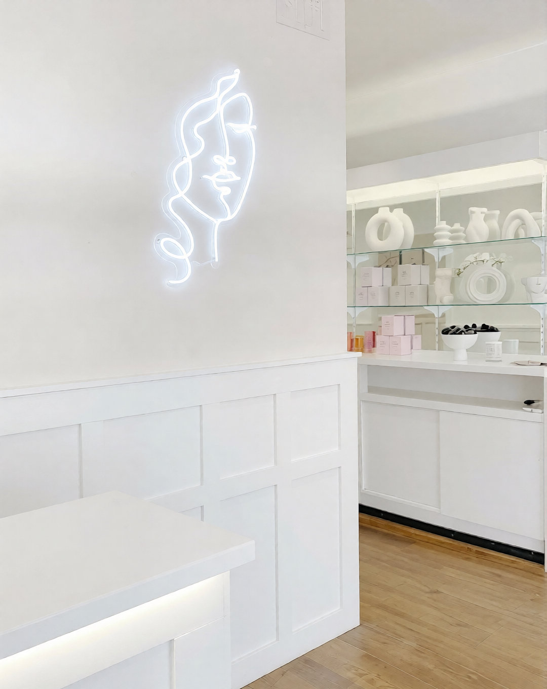 Neon line art face on the studio wall beside the retail shelves